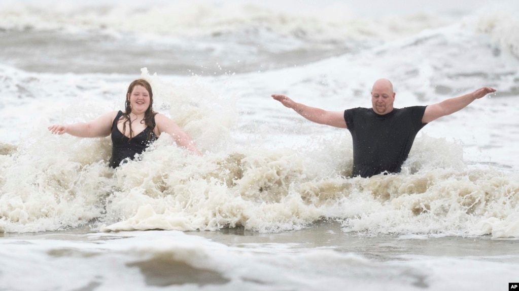 Jeremy Reddout and his daughter, Elexus, enjoy the waves between Murdoch's and Pleasure Pier as rain falls in Galveston, Texas, June 19, 2024.