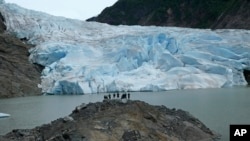 A group of people take in the views of the Mendenhall Glacier on June 8, 2023, in Juneau, Alaska. The glacier in the summer is accessible by kayak or canoe, by foot on a challenging trail or by helicopter. As the Mendenhall Glacier continues to recede, tourists are flooding into Juneau. A record number of cruise ship passengers are expected this year in the city of about 30,000 people. (AP Photo/Becky Bohrer)