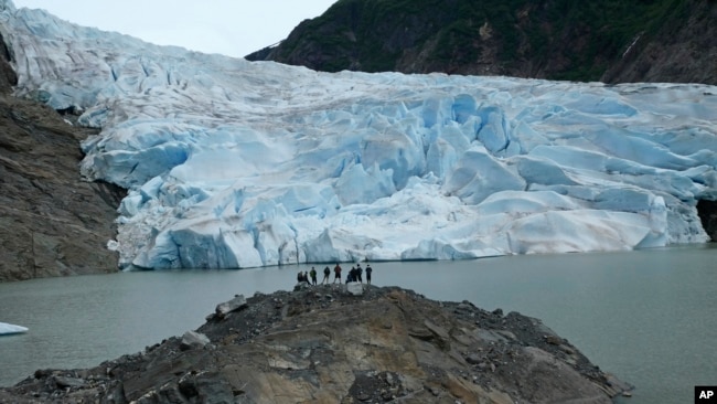 A group of people take in the views of the Mendenhall Glacier on June 8, 2023, in Juneau, Alaska. The glacier in the summer is accessible by kayak or canoe, by foot on a challenging trail or by helicopter. As the Mendenhall Glacier continues to recede, tourists are flooding into Juneau. A record number of cruise ship passengers are expected this year in the city of about 30,000 people. (AP Photo/Becky Bohrer)