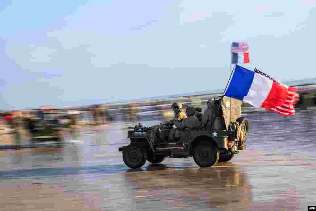 Enthusiasts dressed in replica U.S. Army WWII-era military attire drive a Willys Jeep on Utah Beach, June 6, 2024 during the &quot;D-Day&quot; commemorations marking the 80th anniversary of the World War II Allied landings in Normandy, France.