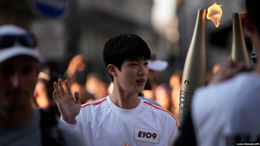 Jin, anggota tertua grup boyband BTS, menerima obor Olimpiade di Paris, Minggu, 14 Juli 2024. Jin akan mewakili Korea Selatan untuk relai obor Olimpiade. (Foto: Louise Delmotte/AP Photo)
