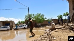 People stand in muddy water after heavy flooding in Baghlan province, in northern Afghanistan, May 12, 2024. Victims of the devastating floods are burying the dead and looking for the loved ones still missing. 