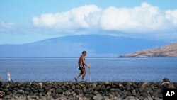 Vicente Rubio walks along a sea wall, Aug. 15, 2023, in Kihei, Hawaii, following wildfires that ravaged Maui.