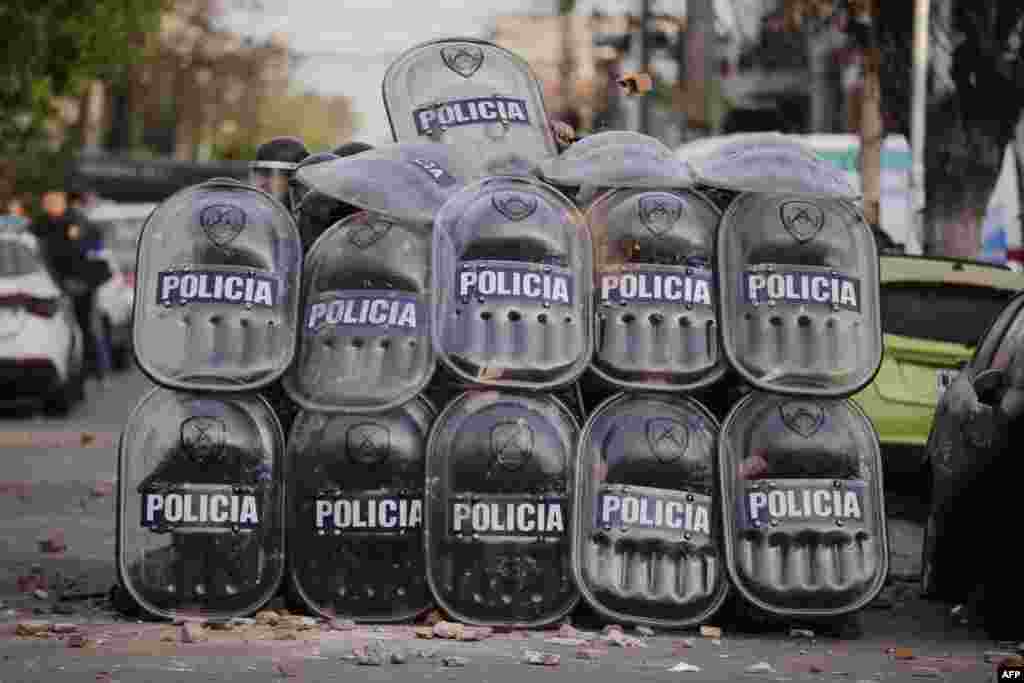 Policemen protect themselves from protesters during a demonstration held by residents of the Lanus municipality demanding justice for an 11-year-old girl who died after being robbed of her backpack and beaten on the way to school, in Lanus, Buenos Aires Province, Argentina, Aug. 9, 2023.