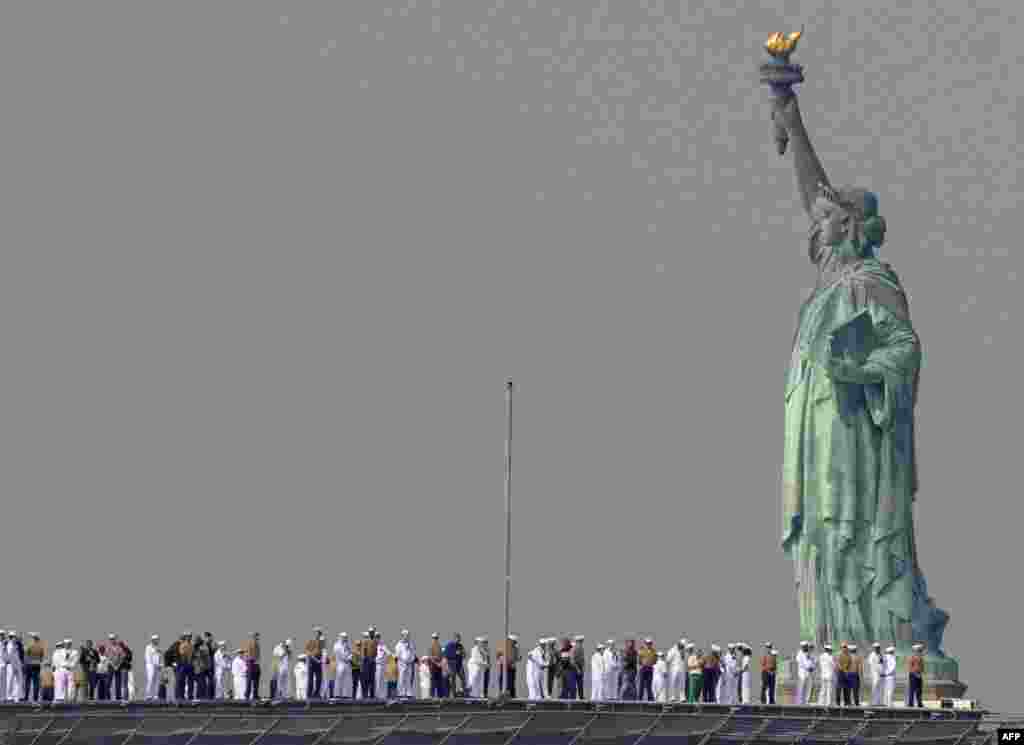 Американските морнари и маринци стојат на палубата на носачот на авиони, додека поминува покрај Статуата на слободата за време на Неделата на флотата во Њујорк.