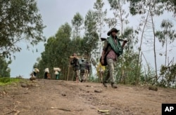 FILE — An unidentified armed militia fighter walks down a path as villagers flee with their belongings in the other direction, near the village of Chenna Teklehaymanot, in the Amhara region of northern Ethiopia, Sept. 9, 2021.