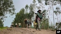 FILE — An unidentified armed militia fighter walks down a path as villagers flee with their belongings in the other direction, near the village of Chenna Teklehaymanot, in the Amhara region of northern Ethiopia, Sept. 9, 2021.