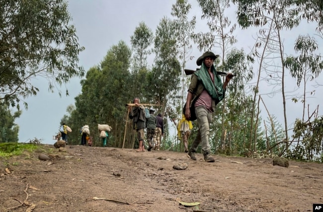 FILE — An unidentified armed militia fighter walks down a path as villagers flee with their belongings in the other direction, near the village of Chenna Teklehaymanot, in the Amhara region of northern Ethiopia, Sept. 9, 2021.