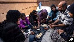 Members of the Abu Jarad family, who were displaced by the Israeli bombardment of the Gaza Strip, eat breakfast at a makeshift tent camp in the Muwasi area, southern Gaza, Jan. 1, 2024.