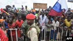 A Nigerien police officer stand guard outside the Niger and French airbases in Niamey as supporters of Niger's National Council for the Safeguard of the Homeland (CNSP), holding a sign and Russian flag, rally, Aug. 27, 2023.