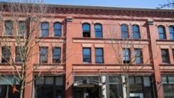 FILE- A person looks out the window as others walk by an affordable housing building.