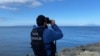 FILE - A Turkish coast guard officer looks through binoculars as a drone searches for victims, after a boat carrying migrants capsized off the Turkish coast, March 15, 2024. (Demiroren News Agency via AFP) 