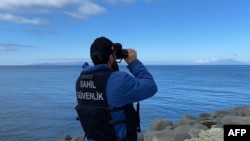 FILE - A Turkish coast guard officer looks through binoculars as a drone searches for victims, after a boat carrying migrants capsized off the Turkish coast, March 15, 2024. (Demiroren News Agency via AFP) 