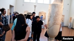 FILE - A group of Chinese tourists listen to a tour guide at the National Archaeological Museum in Athens, Greece, Aug. 3, 2017. 