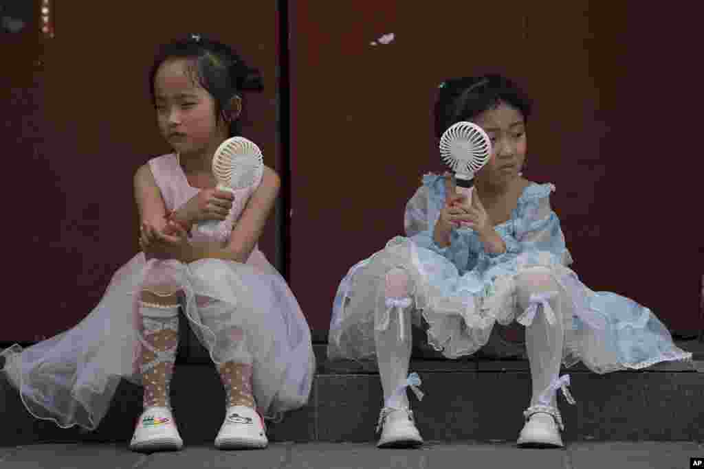 Children cool themselves with electric fans as they take a rest near the Forbidden City on a hot day in Beijing, China, June 25, 2023. 