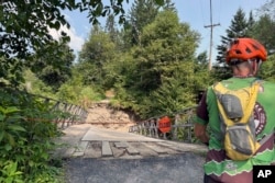 A cyclist looks at a closed flood-damaged bridge at Kingdom Trails in Burke, Vt., Aug. 14, 2024.