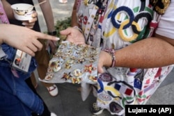 Vivianne Robinson dengan ramah menawarkan salah satu pin koleksinya dari Olimpiade AS 1984 kepada seorang pejalan kaki di Paris. (Foto: AP/Lujain Jo)