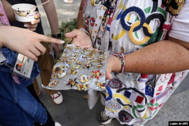 Vivianne Robinson dengan ramah menawarkan salah satu pin koleksinya dari Olimpiade AS 1984 kepada seorang pejalan kaki di Paris. (Foto: AP/Lujain Jo)