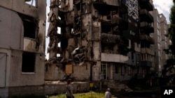 在乌克兰博罗江卡，一名妇女和一名男孩走过一栋在俄罗斯袭击中被毁的公寓楼。(2023年8月2日)