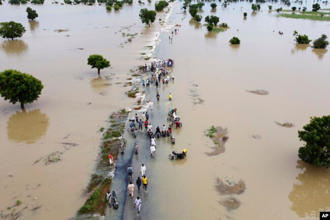 FILE - People walk through floodwaters after heavy rainfall in Hadeja, Nigeria, Sept 19, 2022. A new United Nations report on climate change is being held up by a battle between rich and developing countries over emissions targets and financial aid to vulnerable nations. (AP Photo, File)