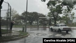 Un transeúnte se refugia bajo un paraguas mientras camina por una acera de Caracas durante una lluvia, el martes 30 de mayo de 2023.