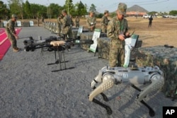 Seorang tentara China (kanan) menguji senjata yang dilengkapi robot sebelum latihan militer Naga Emas (Golden Dragon) di Desa Svay Chock, Provinsi Kampong Chhnang, di utara Phnom Penh, Kamboja, 16 Mei 2024. (Foto: Heng Sinith/AP Photo)