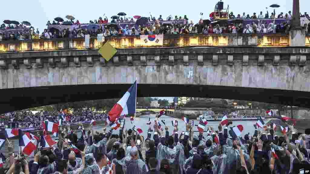 Para atlet Prancis mengibarkan bendera saat menyusuri Sungai Seine dengan perahu pada upacara pembukaan Olimpiade Musim Panas 2024 di Paris, Jumat, 26 Juli 2024. (Foto: Franck Fife/Pool Photo via AP)