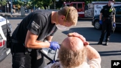 FILE- In this June 26, 2021 file photo a paramedic with Falck Northwest ambulances treats a man experiencing heat exposure during a heat wave, in Salem, Ore. 