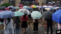 ARCHIVO - Padres y maestros esperan afuera de una escuela donde los estudiantes toman el examen nacional anual de ingreso a la universidad, también conocido como Gaokao, mientras llueve en Beijing, el viernes 7 de junio de 2024.