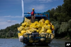 FILE - A volunteer stands on top of a pile of rubbish collected that day while participating in the Plastic Cup event near Tiszaroff, Hungary, Aug. 2, 2023.