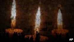 La gente camina junto a una imagen de velas conmemorativas, proyectadas en los muros de la Ciudad Vieja de Jerusalén en la víspera del Día Anual de Conmemoración del Holocausto, el lunes 17 de abril de 2023. Israel celebra el día de conmemoración cada año para recordar a los seis millones de judíos víctimas del genocidio nazi durante la Segunda Guerra Mundial. (Foto AP/Mahmoud Illean)