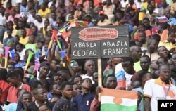 FILE - A man holds a sign reading "Down with France down with ECOWAS" as supporters of the military leaders behind the coup gather at the General Seyni Kountche stadium in Niamey, Niger, Aug. 26, 2023.