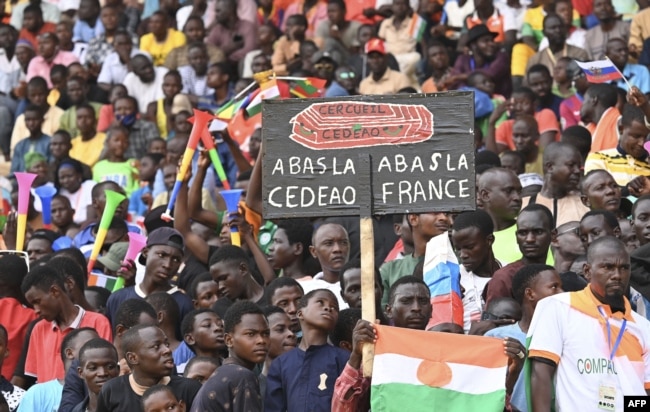 FILE - A man holds a sign reading "Down with France down with ECOWAS" as supporters of the military leaders behind the coup gather at the General Seyni Kountche stadium in Niamey, Niger, Aug. 26, 2023.