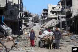 FILE - Palestinians walk past piles of rubble in Khan Younis, Gaza Strip, March 8, 2024.