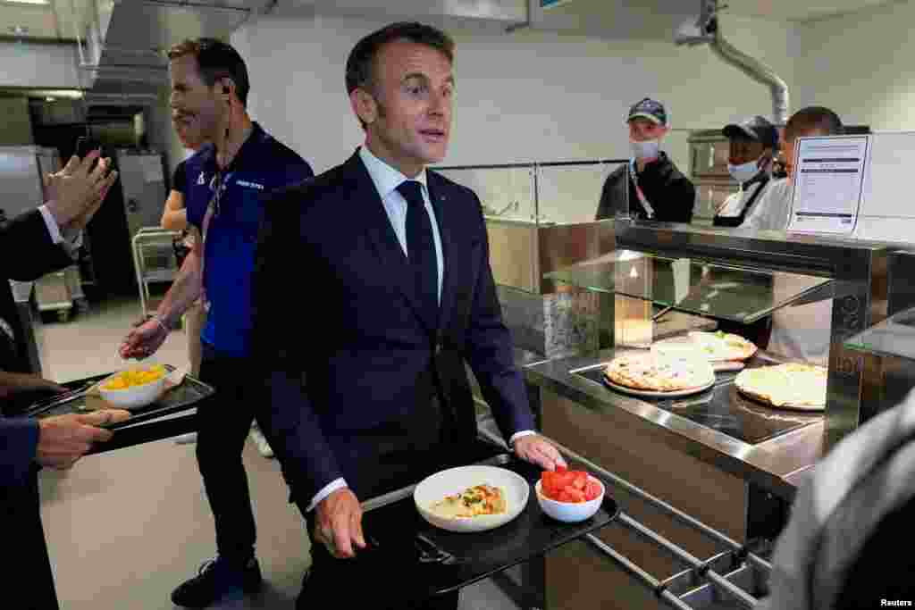 Presiden Prancis Emmanuel Macron memegang piringnya saat mengunjungi desa Olimpiade (Olympic village) untuk Olimpiade Musim Panas 2024, di Paris. (Reuters)&nbsp;