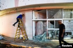 A man walks as another works outside of a damaged building after rockets from Lebanon were fired into Israel, in Shlomi, northern Israel, April 6, 2023.