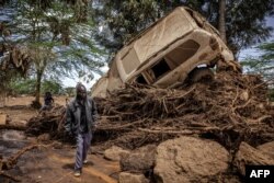 Seorang pria berjalan di dekat mobil yang rusak di daerah yang terkena dampak hujan lebat dan banjir bandang di desa Kamuchiri, dekat Mai Mahiu, 29 April 2024.(LUIS TATO / AFP)