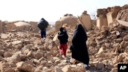 An Afghan woman walks with her children amid debris after a powerful earthquake in Herat province, western of Afghanistan, Oct. 15, 2023, in this handout photo released by Save the Children.