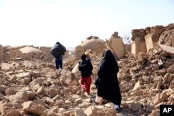 An Afghan woman with her children walk amid debris after a powerful earthquake in Herat province, western of Afghanistan, Oct. 15, 2023, in this handout photo released by Save the Children. (Photo via AP)