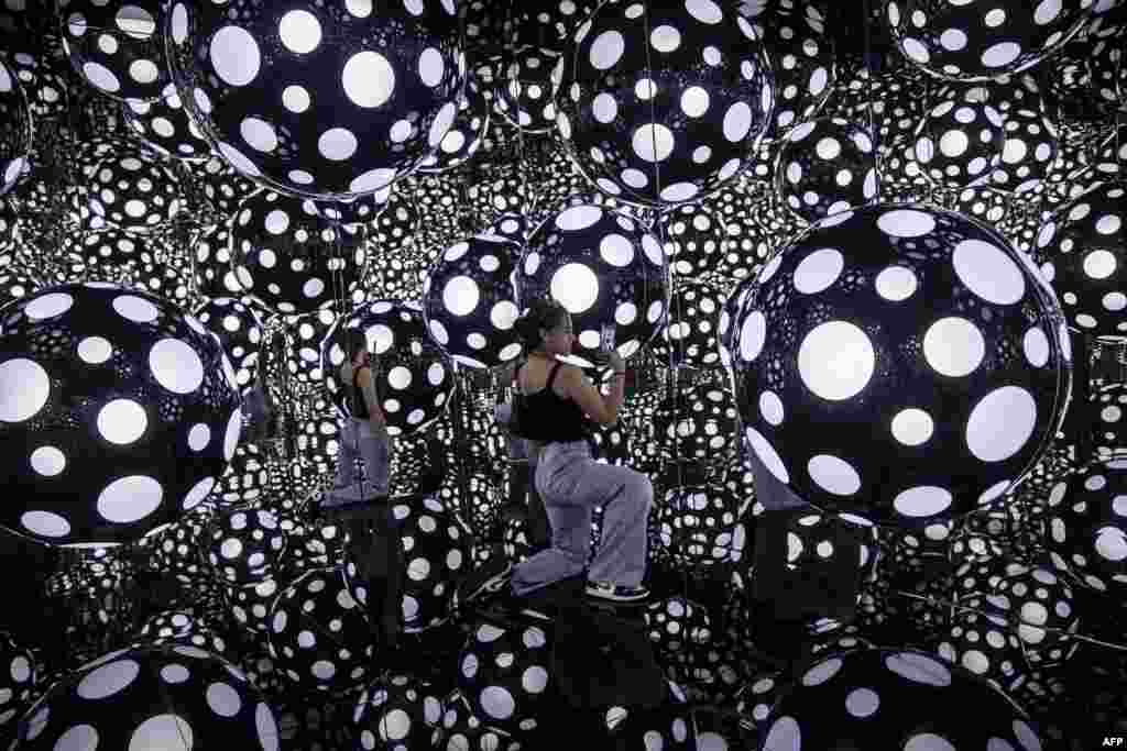 A woman takes photos at an art installation called Dots Obsession - Aspiring to Heavens Love by artist Yayoi Kusamas with her signature polka dots and reflective mirrors, in Hong Kong.