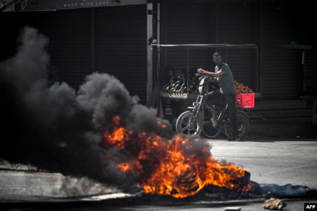 Palestinians look on behind burning tires during an Israeli raid in the occupied West Bank city of Jenin on May 21, 2024.