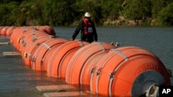 FILE - A kayaker walks past large buoys being used as a floating border barrier on the Rio Grande, Aug. 1, 2023, in Eagle Pass, Texas.