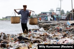 Seorang lelaki lanjut usia berjalan melewati tumpukan sampah di sebuah pantai di perkampungan nelayan Teluk, Pandeglang, Banten, 15 Maret 2024. (Foto: REUTERS/Willy Kurniawan)