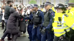 In this photo taken from video, British police officers push back protesters who were seeking to stop the transfer of asylum seekers from a hotel in southeast London to a barge off southern England.