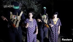 Jočevid Lifšic i Nurti Kuper, koje su militanti palestinskog Hamasa držali u zatočeništvu, hodaju pored maskiranih pripadnika palestinskih milicija, na fotografiji napravljenoj od video snimka i objavljenoj 23. oktobra 2023.