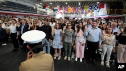 People raise their right hands as they take the Oath of Allegiance to the United States of America during a naturalization ceremony aboard the USS Bataan on May 7, 2024, in Miami.