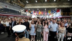 Pessoas levantam a mão direita ao prestarem o Juramento de Fidelidade aos Estados Unidos da América durante uma cerimónia de naturalização a bordo do USS Bataan em 7 de maio de 2024, em Miami.