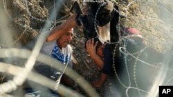 Migrants who crossed the Rio Grande from Mexico to the US work their way through concertina wire, Sept. 22, 2023, in Eagle Pass, Texas.