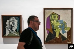 Seorang pria berjalan melewati dua lukisan karya Pablo Picasso di Museum Reina Sofia, Madrid, Spanyol, Senin, 12 September 2022. (AP/Andrea Coma)