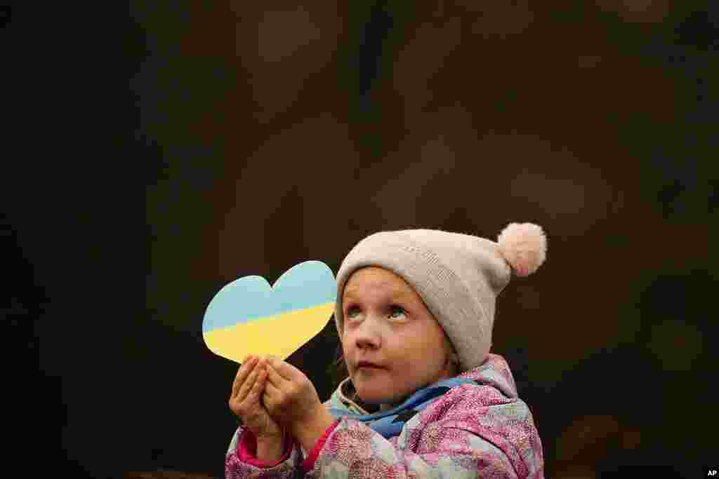 Seorang gadis kecil memegang guntingan berbentuk hati dengan warna bendera Ukraina, selama aksi protes menentang invasi Rusia di Ukraina, menandai peringatan pertama invasi besar-besaran Rusia ke Ukraina, di Bukares, Rumania.